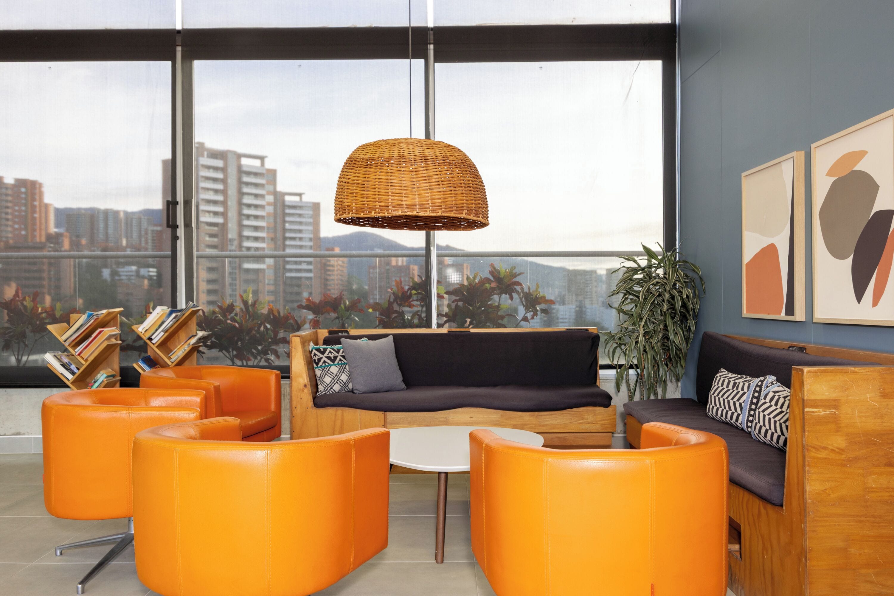 A modern lounge with orange seating, a woven pendant light, and a city view through large windows.