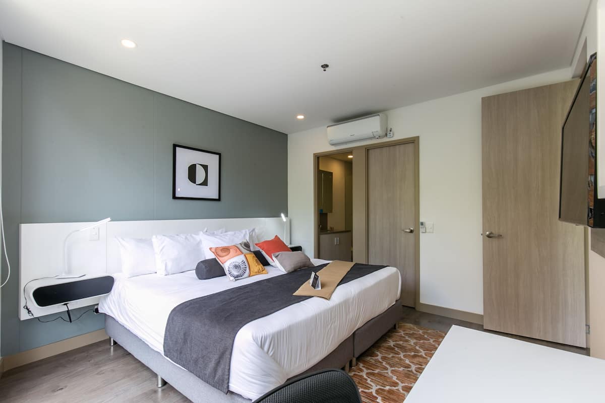 A modern hotel room with a large bed, bedside table, and a wardrobe.