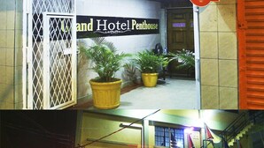 Entrada de hotel con un cartel que dice "Grand Hotel Penthouse", una entrada con portón, plantas en macetas, una escalera y un cartel de "No Estacionar".