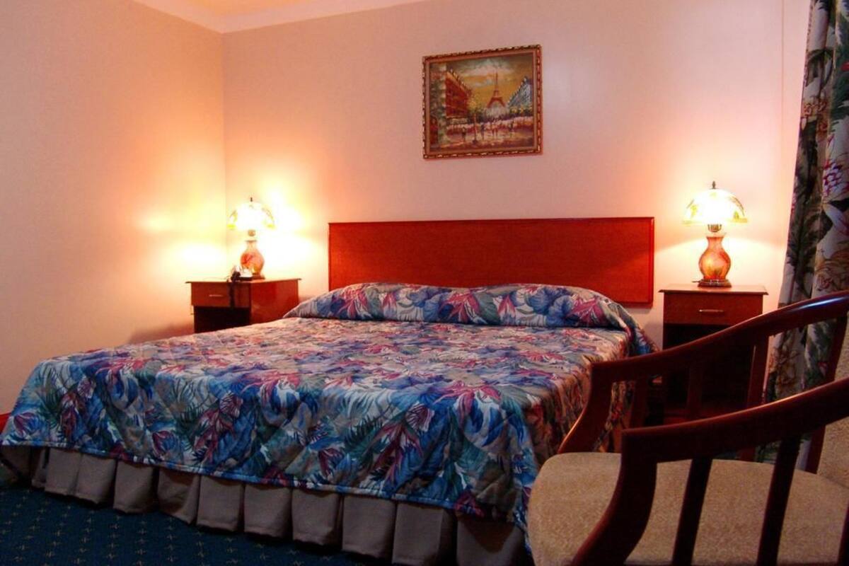 A hotel room with a bed, two bedside tables, a chair, a painting on the wall, and a curtain.