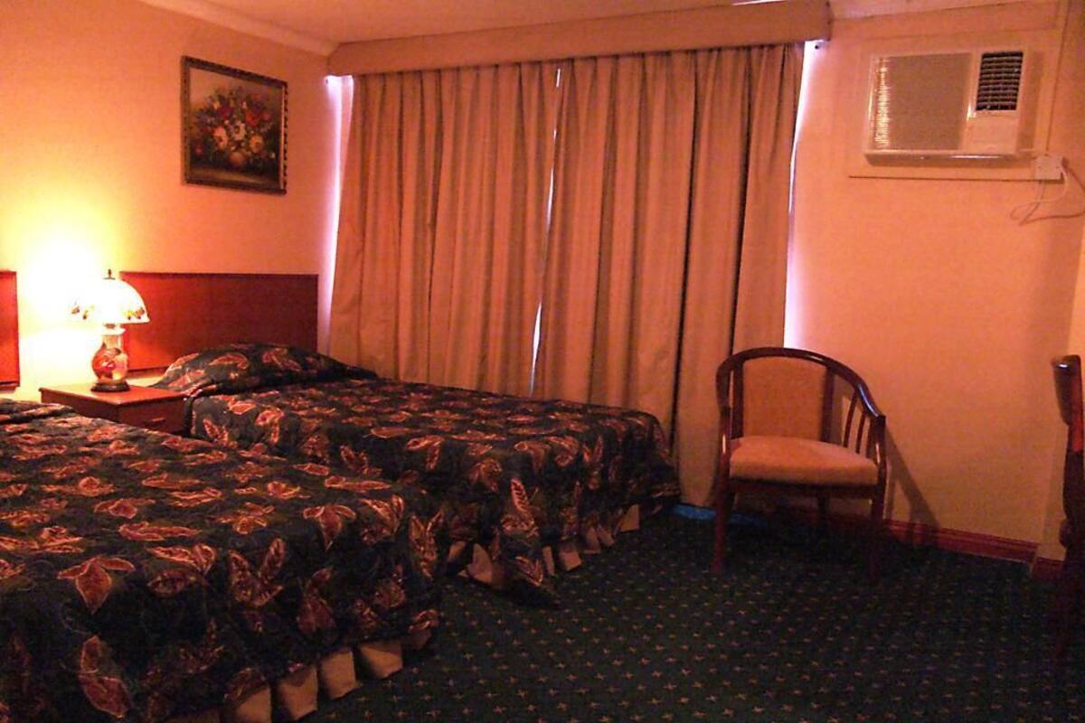 A hotel room with two beds, a chair, a lamp, and a window with curtains.