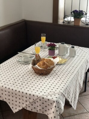 A dining table with a white tablecloth, a basket of bread, a pitcher, a small potted plant, and two glasses of orange juice. - Pension miracle (Zell am See)