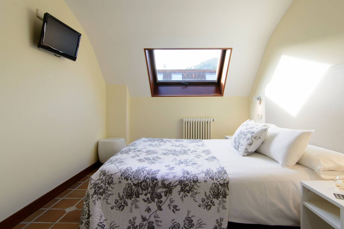 A bedroom with a bed, a window, a radiator, and a television on the wall.