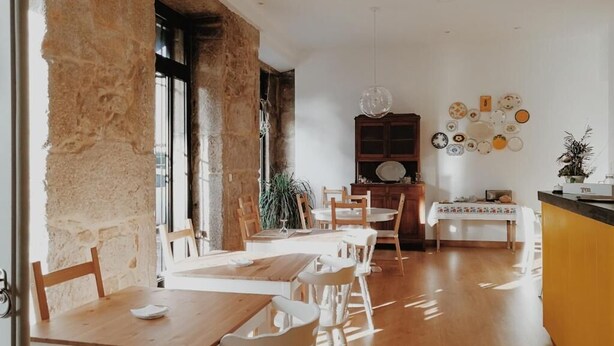 A dining area with wooden tables and chairs, a kitchen area with a yellow counter, and a wall decorated with plates. - Casa do Marqués (Baiona)