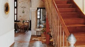 A spacious interior with a wooden staircase leading to an upper level, a stone wall, and a dining area with a table and chairs. - Casa do Marqués (Baiona)