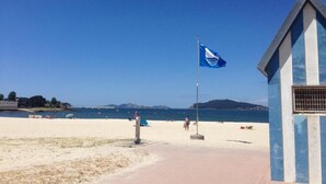 A beach with a flagpole, a small building, and a clear blue sky. - Casa do Marqués (Baiona)