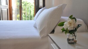 A hotel room with a bed, white bedding, a vase with flowers, and a view of greenery outside. - Casa do Marqués (Baiona)