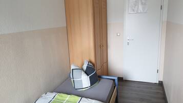 Een eenpersoonsbed met een houten hoofdeinde, een grijze matras en een groen-wit geruit deken.