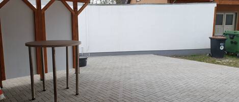 Un patio techado con suelo de dibujo en espiga, una mesa redonda y un cubo de basura verde.