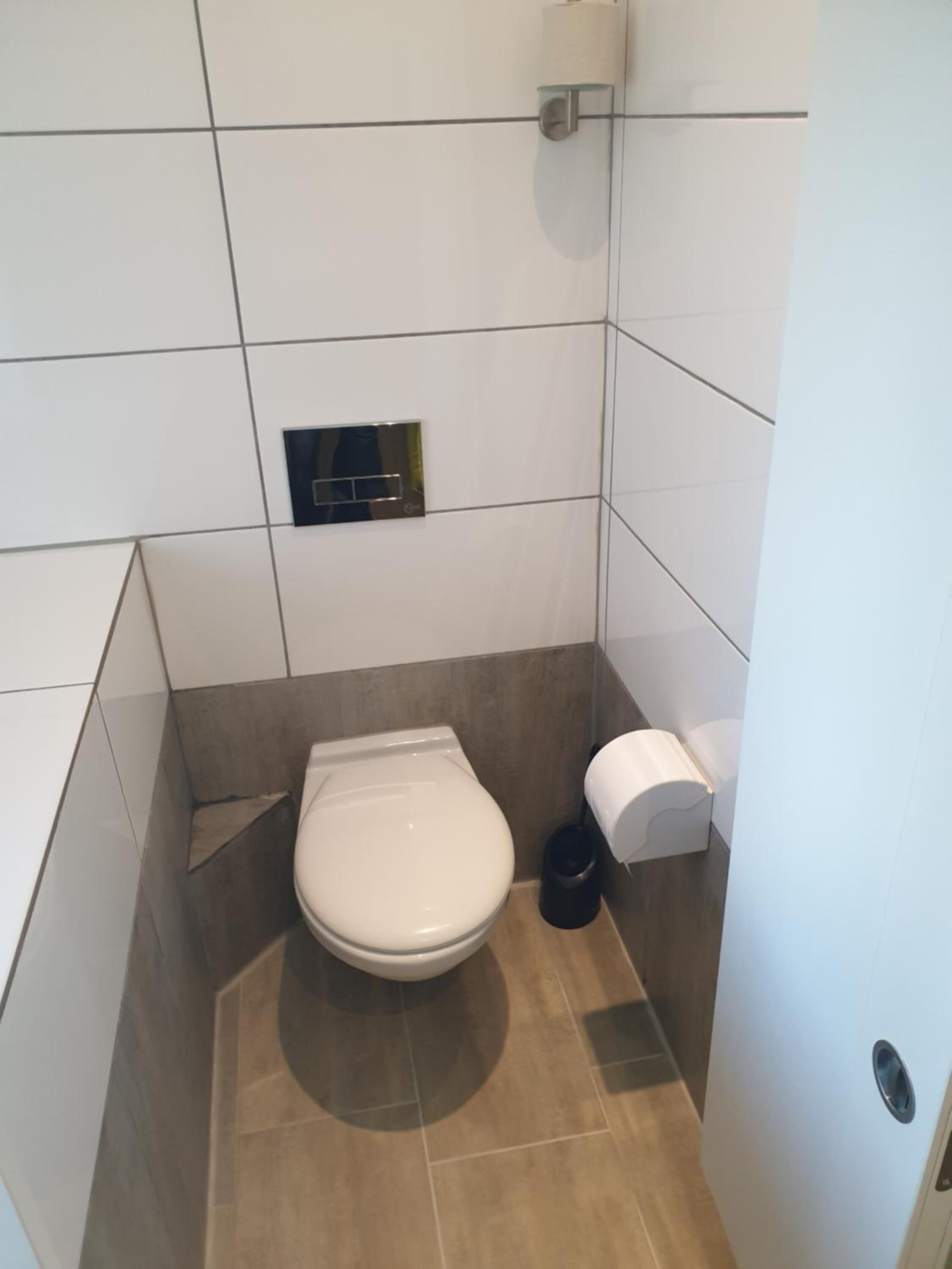 Un baño pequeño y moderno con inodoro, un cesto de basura y dispensador de toallas de papel.