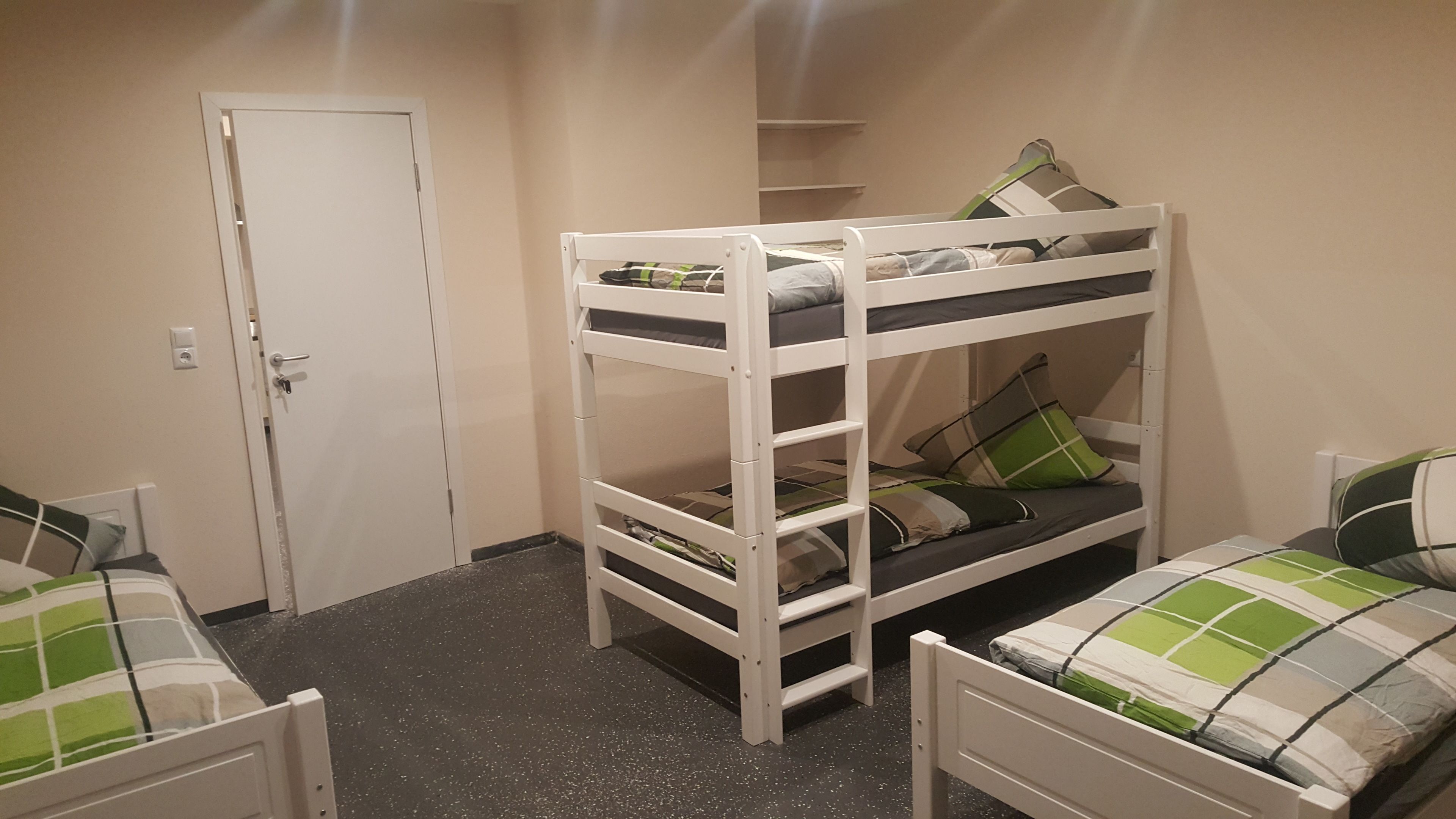 A bunk bed room with a door, a small shelf, and a carpeted floor.