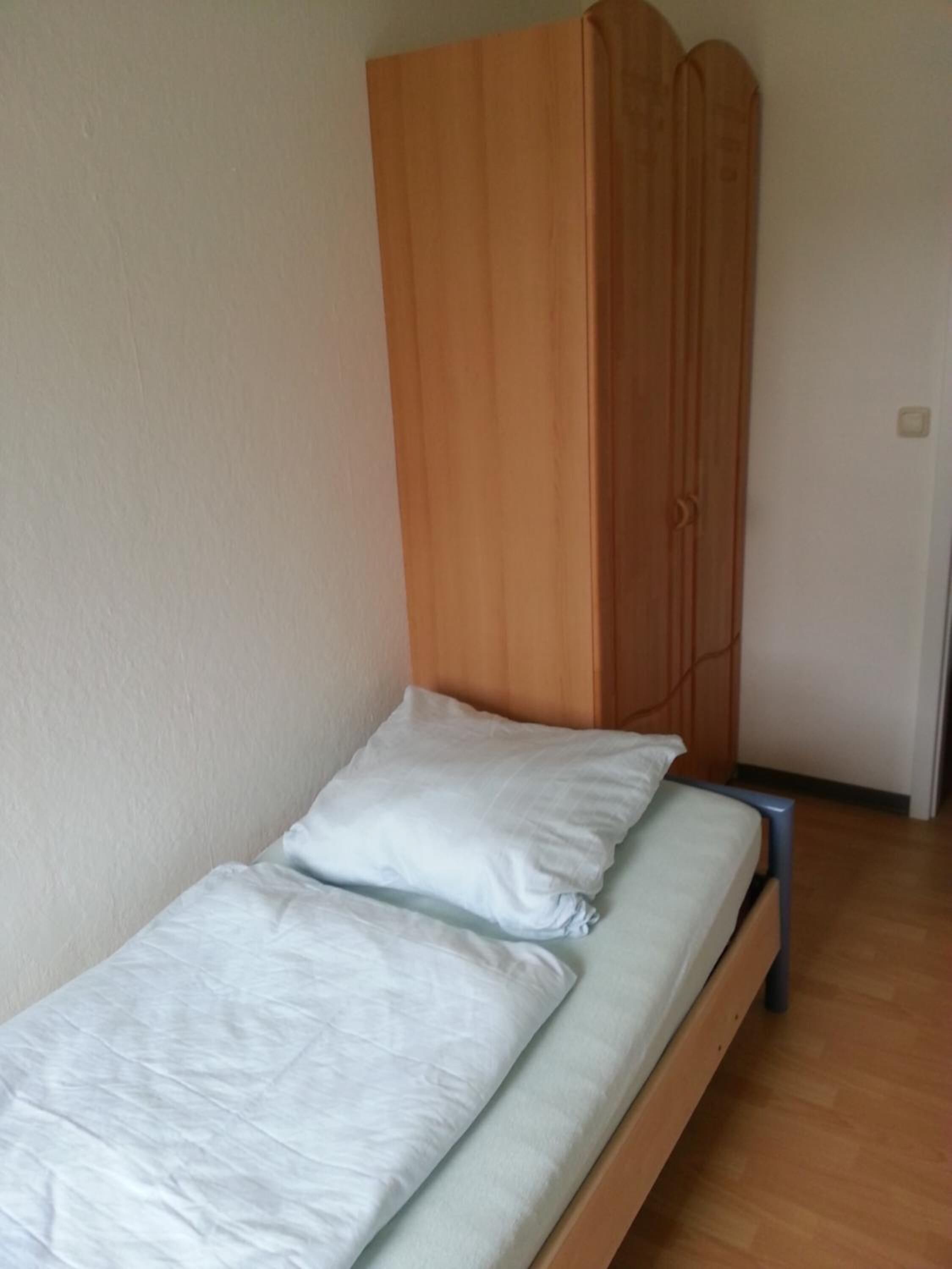 A single bed with a wooden headboard and a white mattress.
