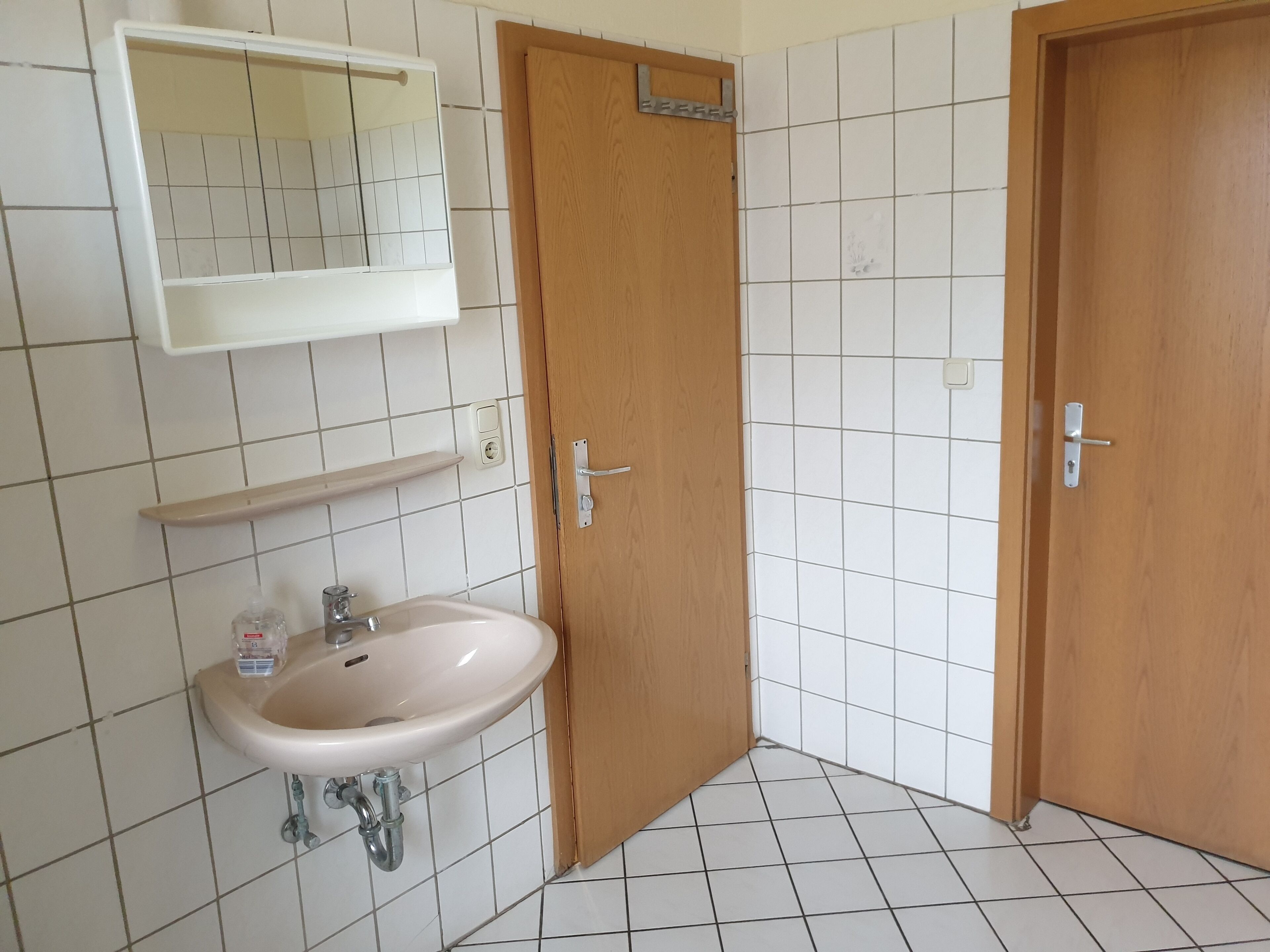 Un baño con lavamanos blanco, puertas de madera y un espejo sobre el lavamanos.