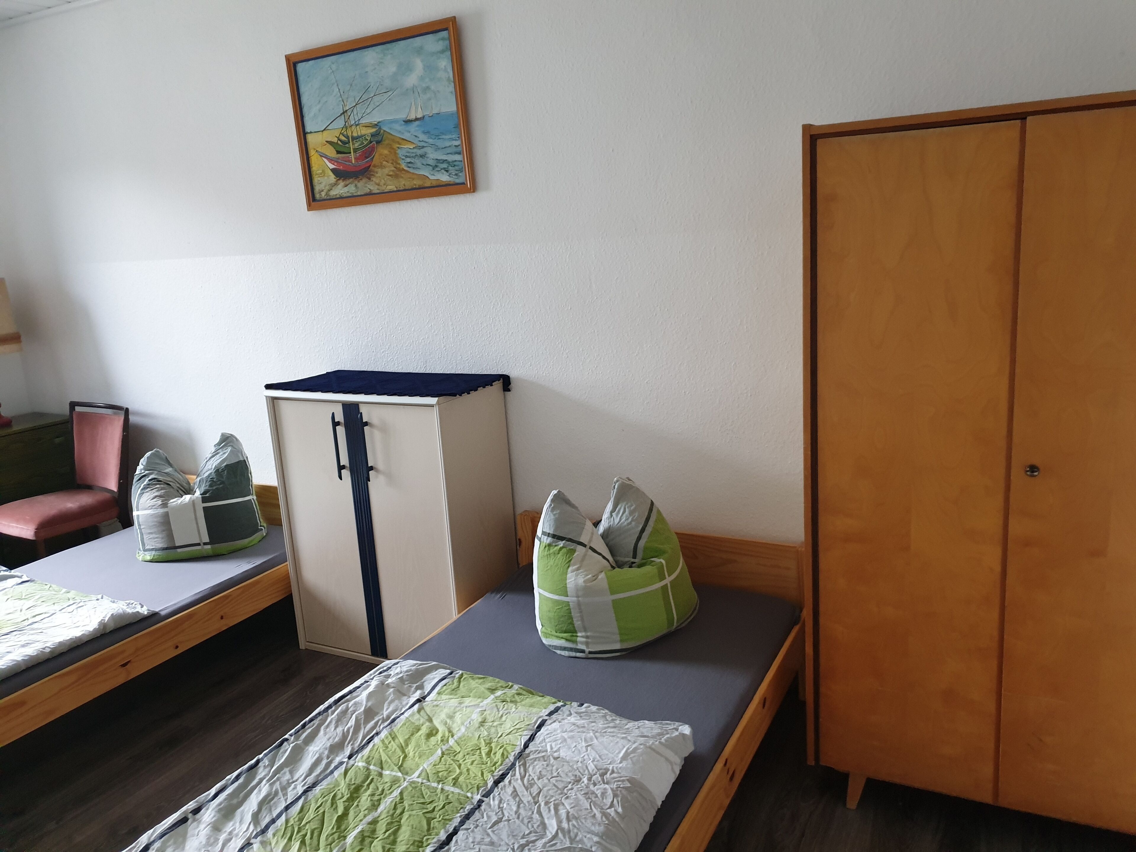 A room with a bunk bed, a wardrobe, a desk, a chair, and a painting on the wall.