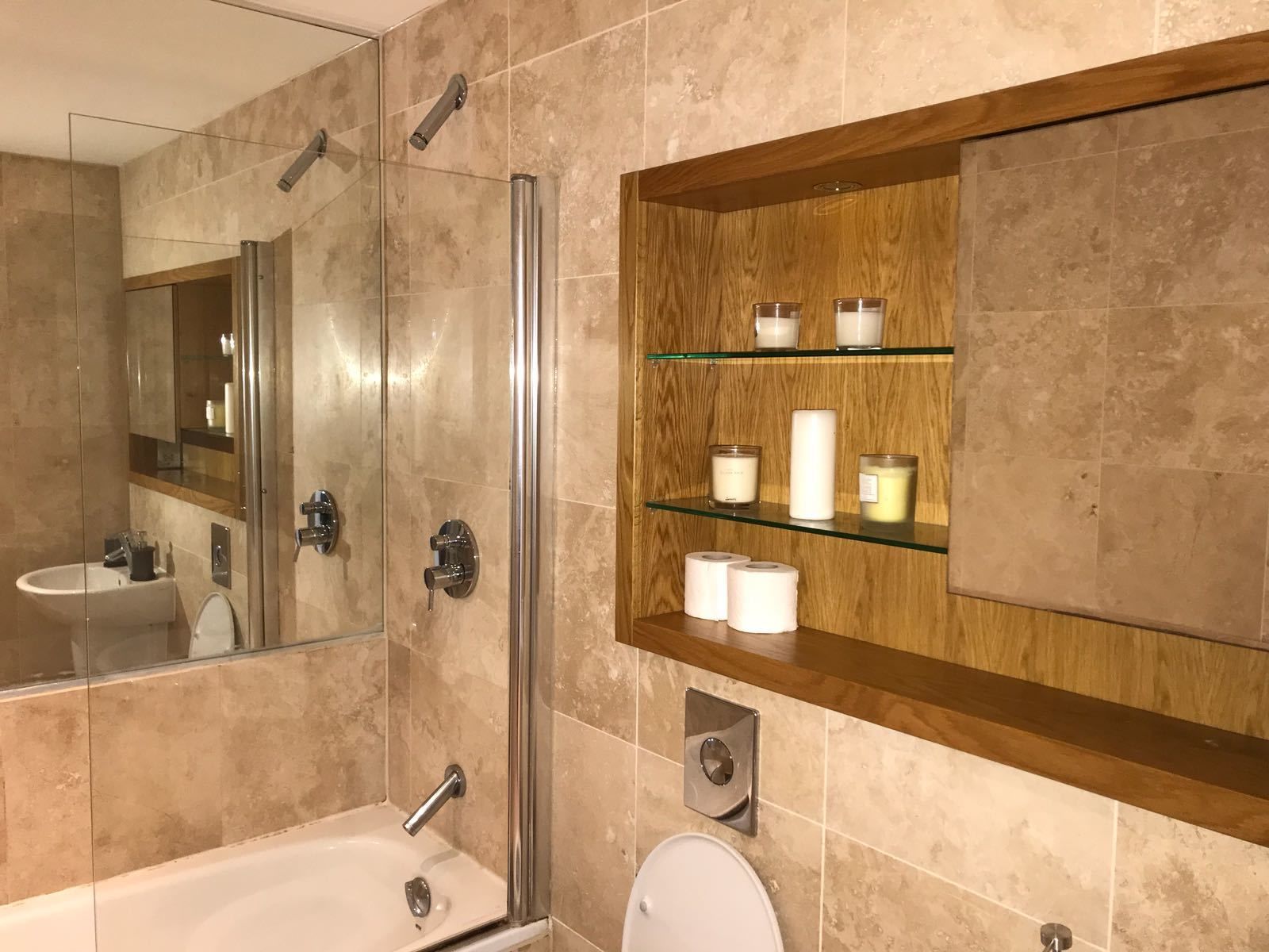 Een moderne badkamer met een douchecabine van glas, een badkuip, een toilet en een wastafel met een spiegel en planken met toiletartikelen.