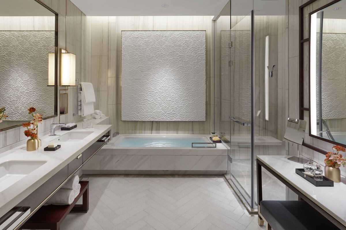 Une salle de bain moderne dotée d’une grande baignoire, de deux lavabos et d’une douche à parois de verre.