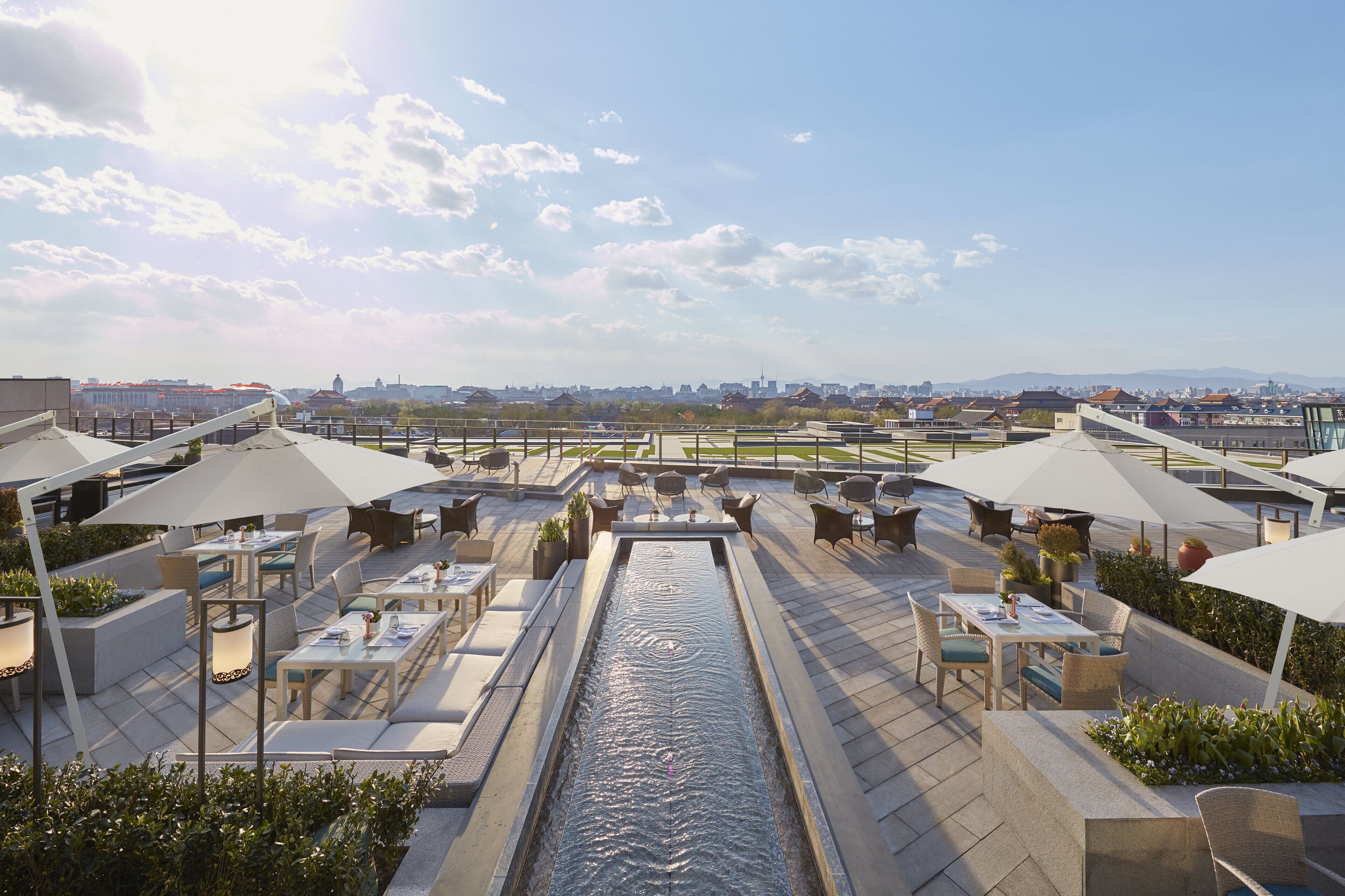 Una terraza en la azotea con mobiliario exterior, una fuente de agua y vistas panorámicas de la ciudad.