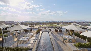 Una terraza en la azotea con mobiliario exterior, una fuente de agua y vistas panorámicas de la ciudad.