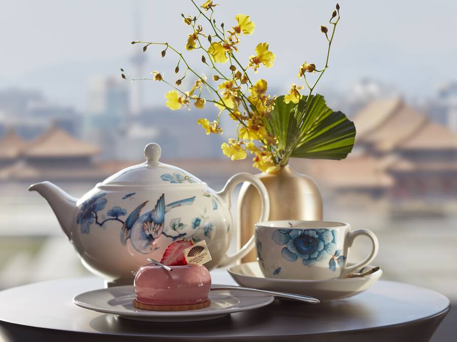 A table with a teapot, cup, saucer, and a small dessert with a strawberry on it.