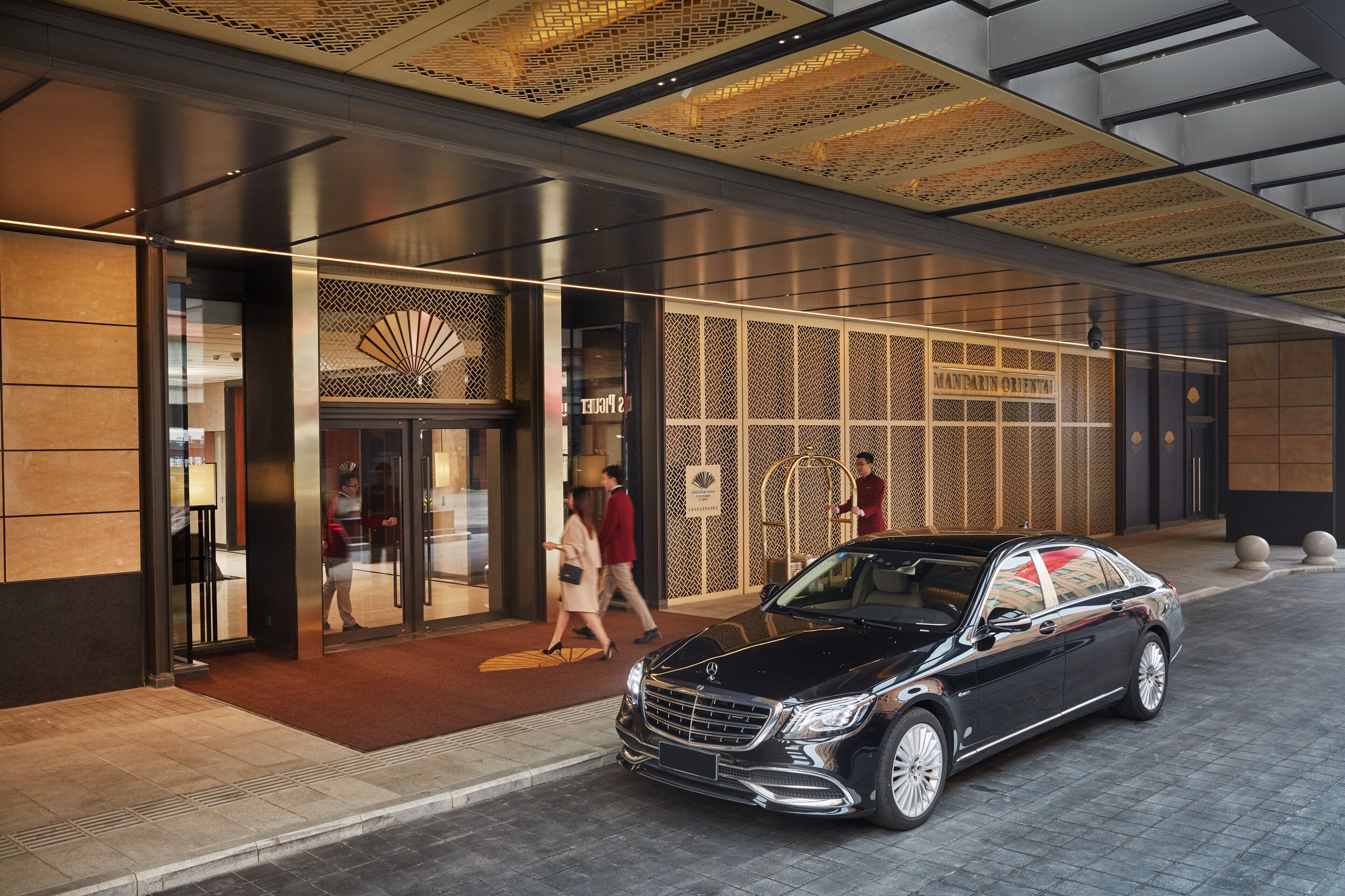 A modern building entrance with a car parked in front, a glass door, and a decorative ceiling.