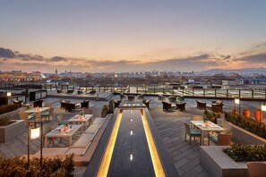 A rooftop terrace with tables and chairs, a central water feature, and a cityscape view in the background. - Mandarin Oriental Wangfujing, Beijing (Beijing)