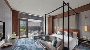 Un hotel moderno con una cama grande, una zona de estar con sofá y sillón, televisión y un ventanal con vistas al exterior.