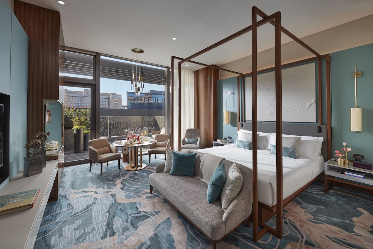 Une chambre d’hôtel moderne dotée d’un lit à baldaquin, d’un canapé, d’un coin repas et d’une grande fenêtre donnant sur la ville.