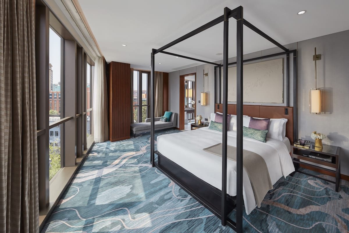 Une chambre d’hôtel moderne avec un lit à baldaquin, de grandes fenêtres, une vue sur la ville et une moquette à motifs bleus.