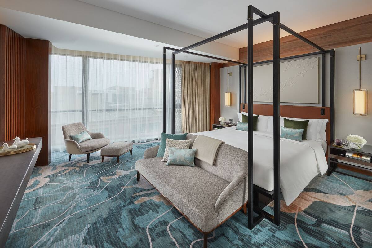 Une chambre d’hôtel moderne avec un lit à baldaquin, un canapé, un fauteuil et une grande fenêtre avec des rideaux.