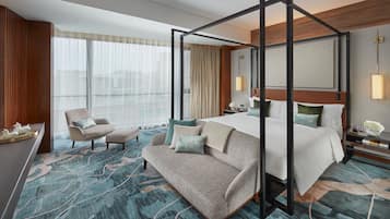 Quarto de hotel moderno com cama de dossel, sofá, poltrona e uma grande janela com cortinas.