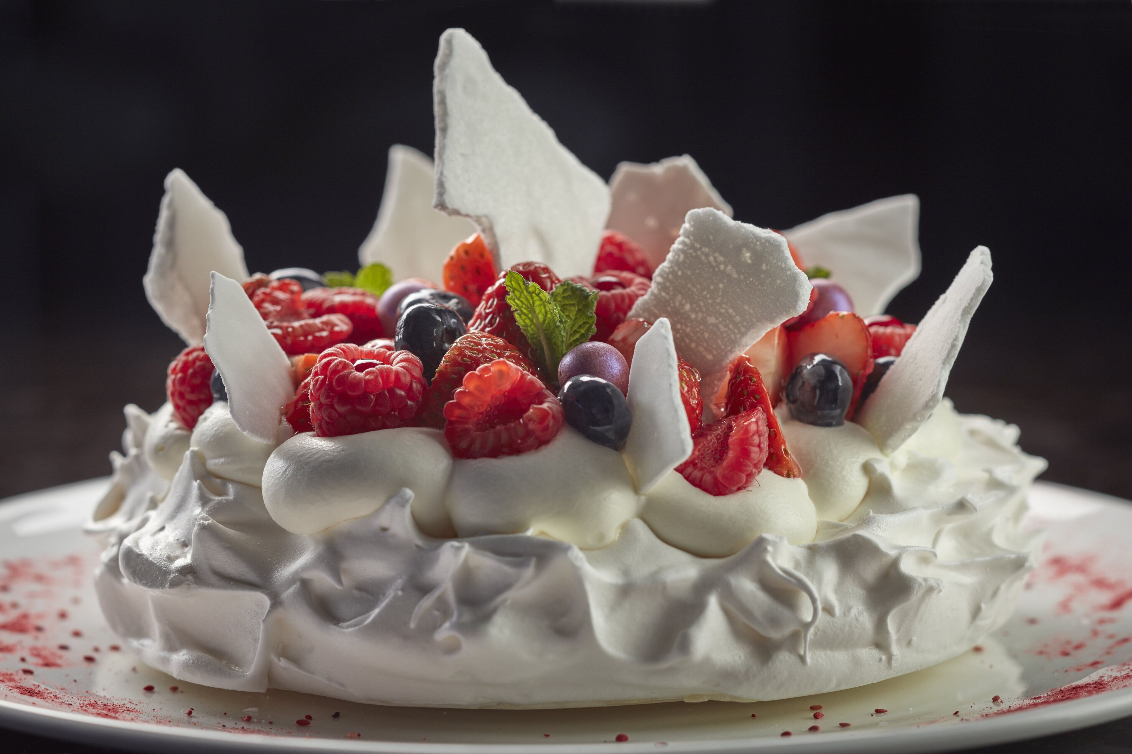 A dessert with whipped cream, strawberries, raspberries, and blueberries, garnished with a chocolate piece.
