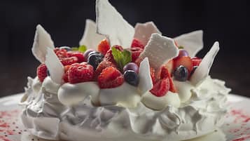 A dessert with whipped cream, strawberries, raspberries, and blueberries, garnished with a chocolate piece.
