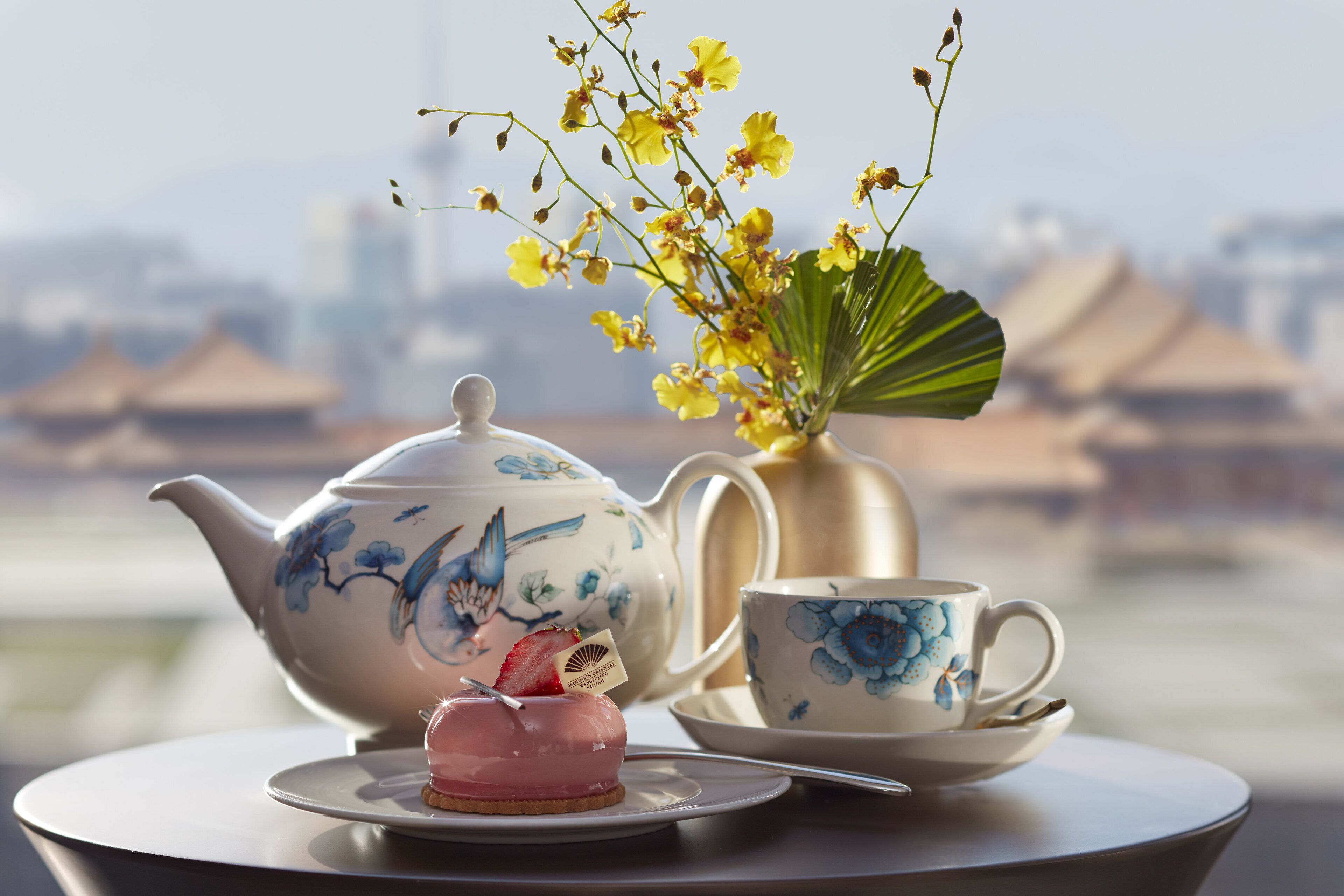 Un tavolo con teiera, tazza, vaso di fiori e un dessert su un piatto.