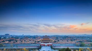 A traditional Chinese architectural complex with multiple buildings, a large open courtyard, and a view of the surrounding cityscape.
