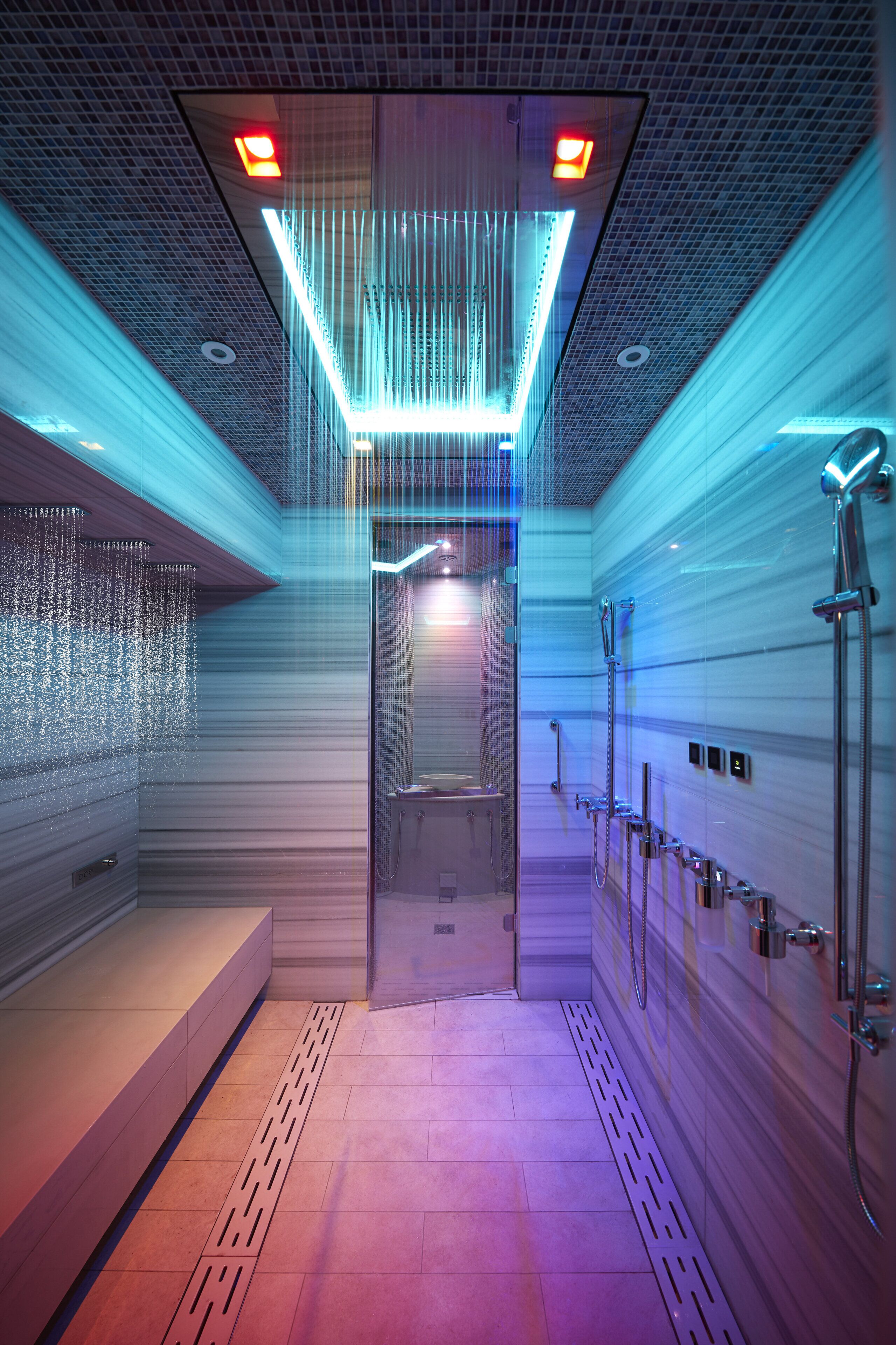 A modern bathroom with a glass-enclosed shower, a bench, and a row of sinks.