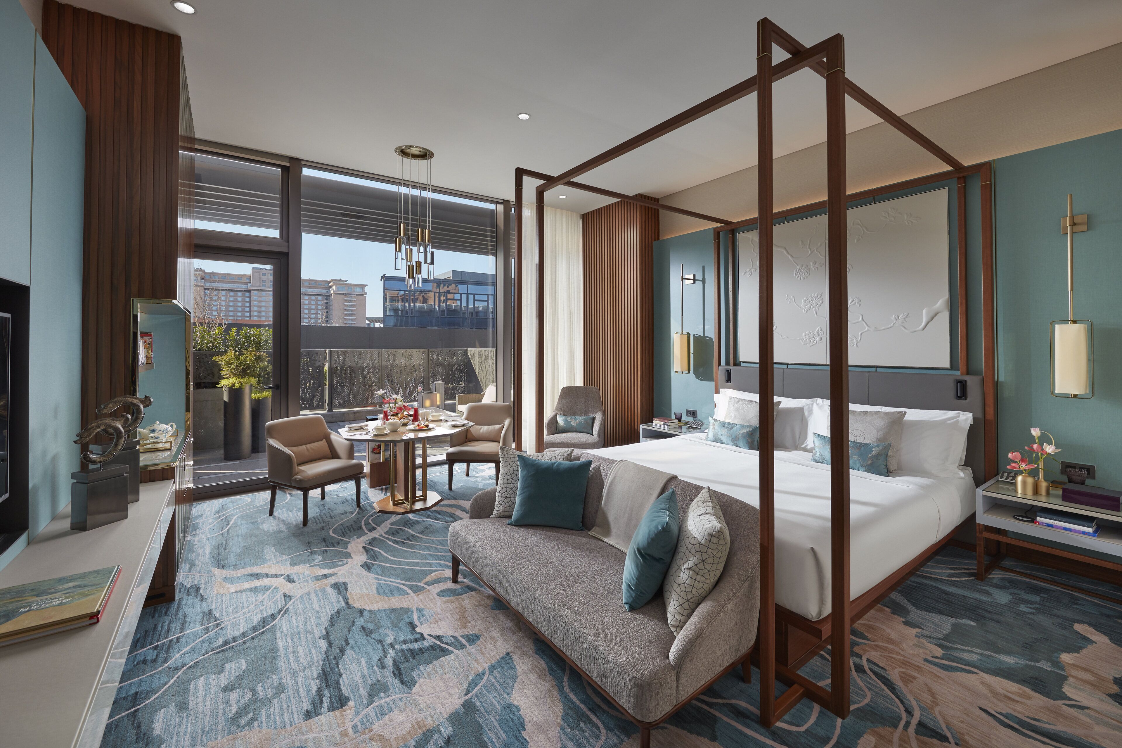 Habitación de hotel moderna con cama con dosel, zona de estar con sofá y sillones, una mesa de comedor y vistas a la ciudad a través de amplias ventanas.