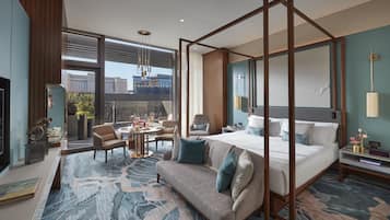 A modern hotel room with a four-poster bed, a sitting area with a sofa and chairs, a dining table, and a view of the cityscape through large windows.