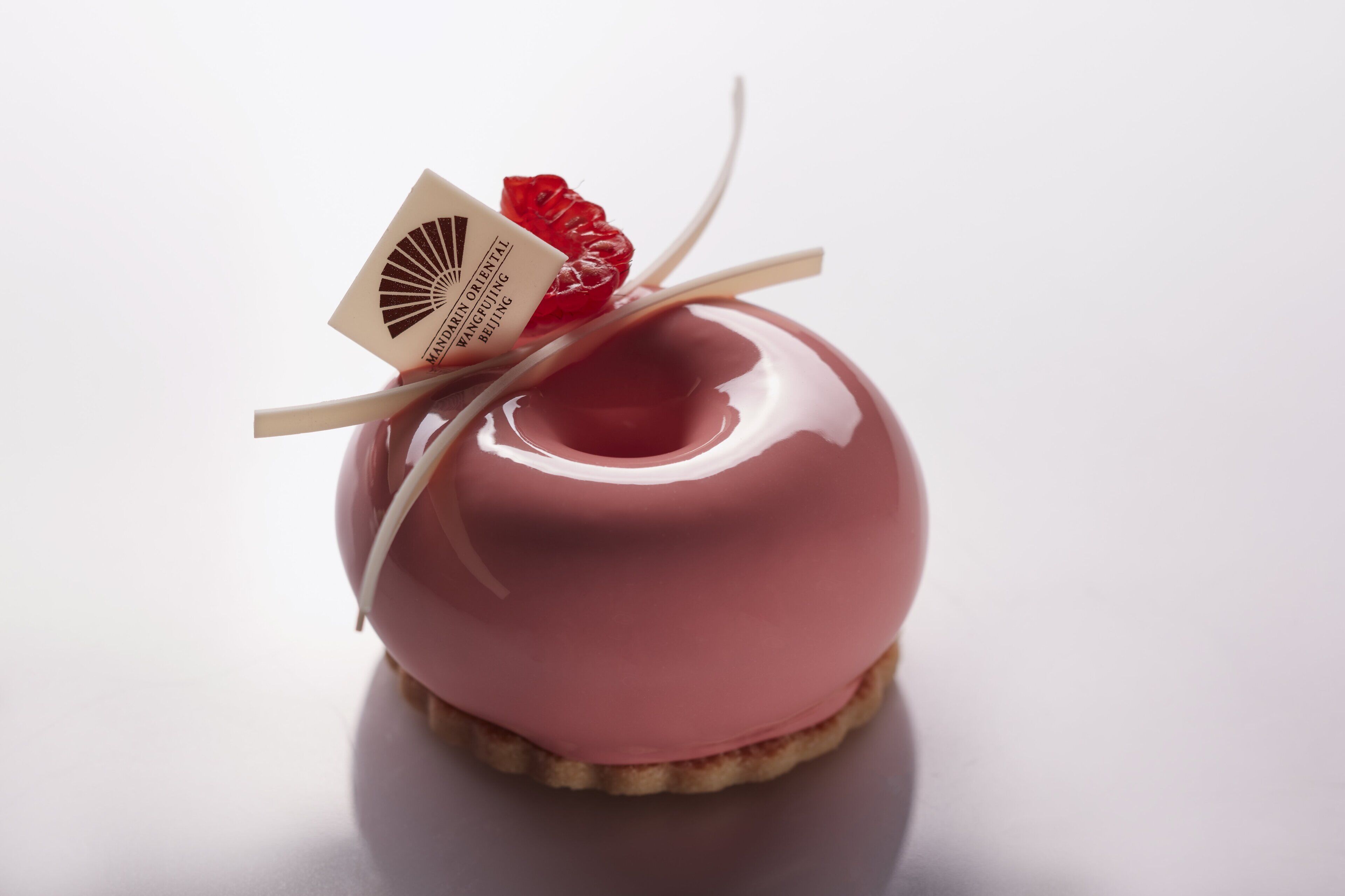 A glossy red apple-shaped dessert with a label and a small red fruit decoration.