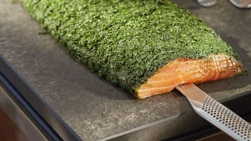 Une assiette de sushis avec une grande tranche de saumon posée sur un lit d’algues vertes, accompagnée d’un couteau et de deux cuillères sur une surface sombre.