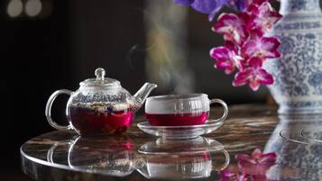 A teapot and cup on a reflective surface with a blurred vase of flowers in the background.