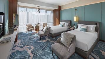 A hotel room with two beds, a sitting area with a chair, a small table, and a television.