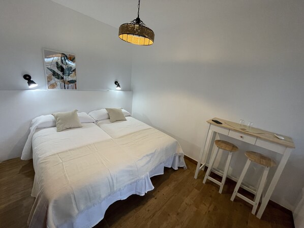A bedroom with a bed, a desk with two chairs, a hanging light fixture, and wall-mounted lamps.