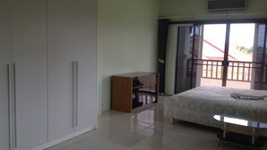 Un dormitorio con cama, armario, pequeño mueble de madera y puerta corrediza de vidrio que da a un balcón.