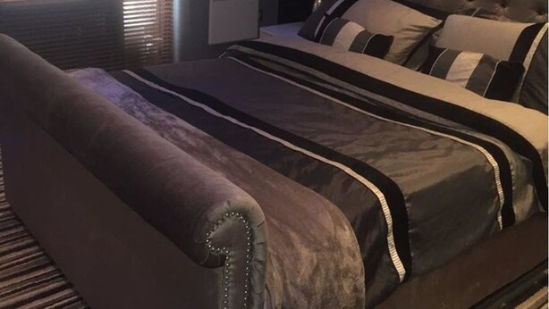 Ein Schlafzimmer mit einem großen Bett, einem dunkelgrauen Sofa und einem Fenster mit Jalousien.