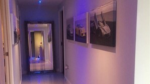 Ein Flur mit weißem Boden und Wänden, einer Tür am Ende sowie drei gerahmten Bildern an der Wand.