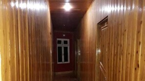 A narrow hallway with wooden walls and a wooden floor, leading to a door with a red frame. - The Park Hotel (Kurseong)