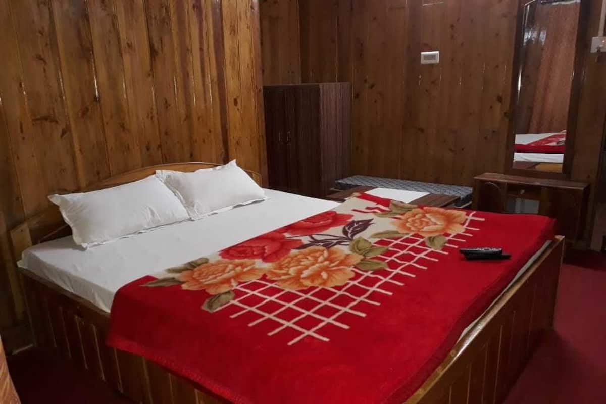 Una cama de madera con almohadas blancas y una colcha estampada de flores rojas.