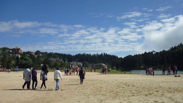 A sandy beach with people walking and a lake in the background. - The Park Hotel (Kurseong)