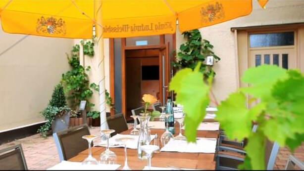 Un espace de restauration en plein air avec des tables pour deux personnes, des parasols jaunes et des plantes en pot.