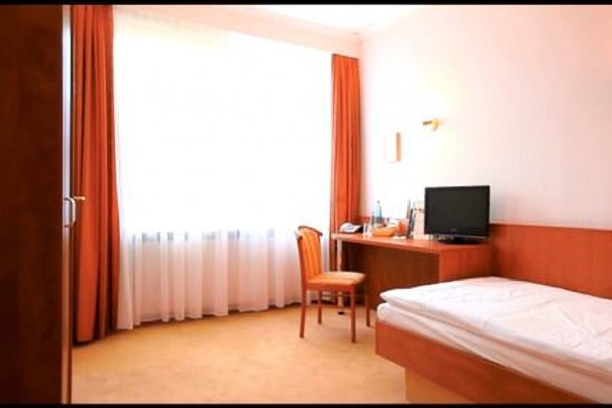 A hotel room with a single bed, a desk with a computer, a chair, and a TV.
